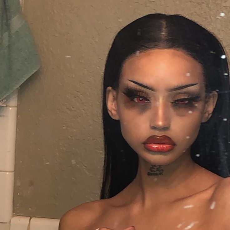 a woman with makeup on her face standing in front of a bathroom mirror and looking at the camera