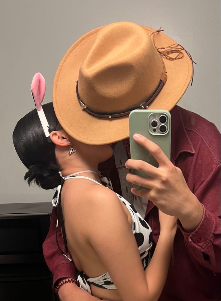 a woman taking a selfie with her cell phone while wearing a hat and bunny ears