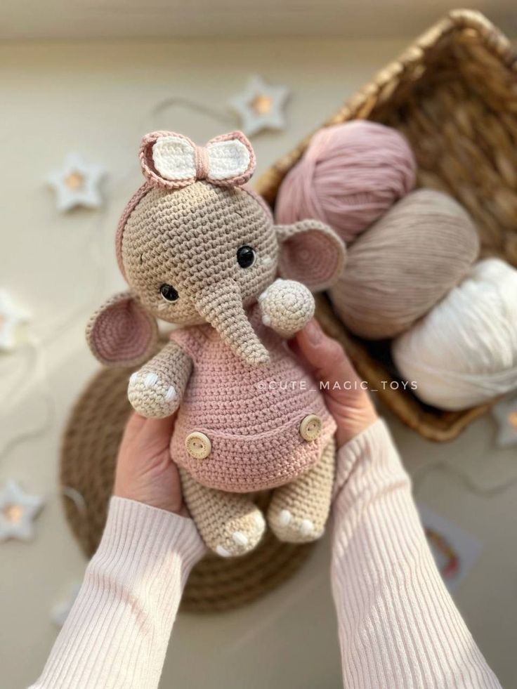 a person holding a small crocheted elephant in front of some balls of yarn