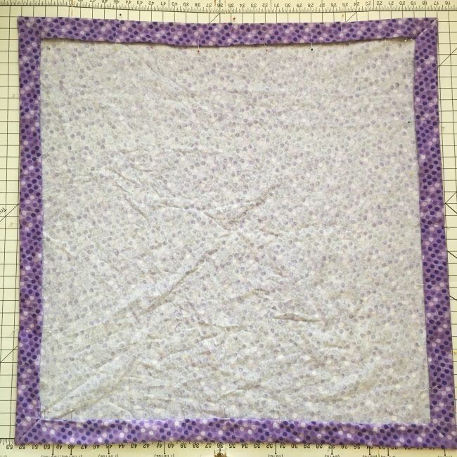 a quilted square with purple trim on it