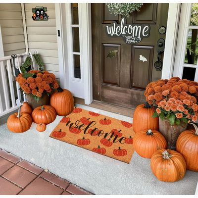 some pumpkins and flowers are sitting on the front porch with welcome mat in front