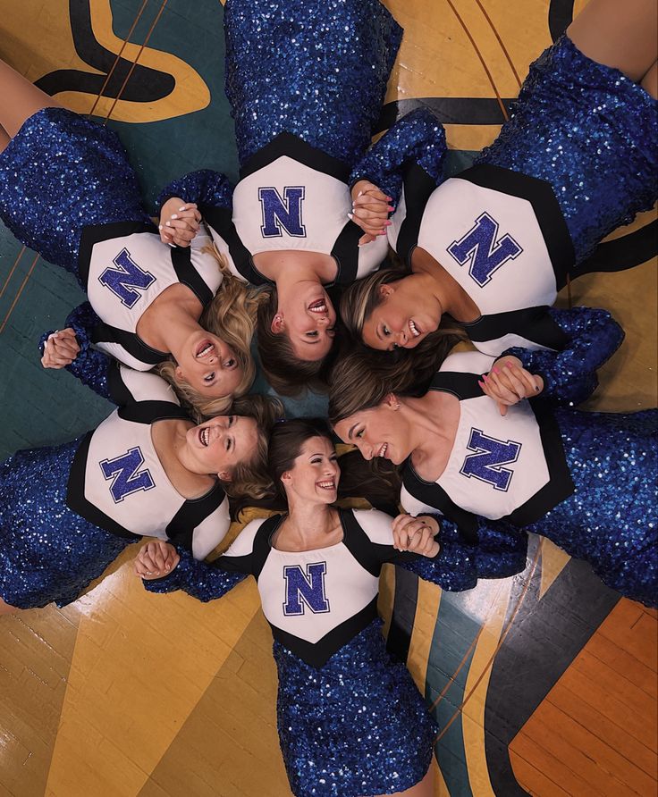 four cheerleaders standing in a circle with their arms around each other and looking at the camera