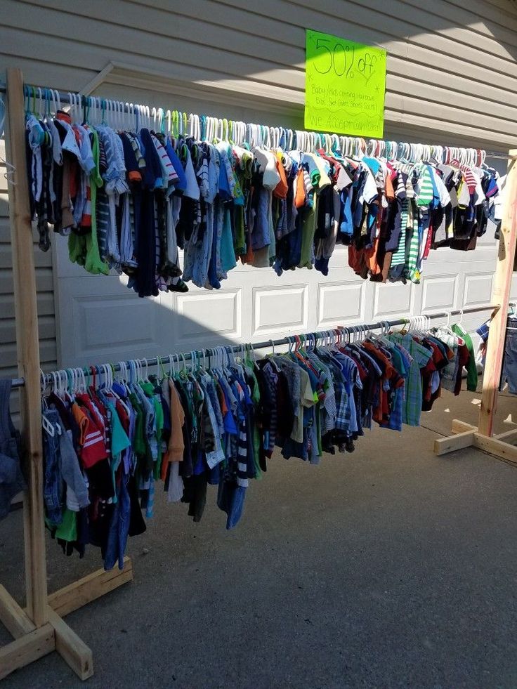 an outdoor clothing rack with clothes hanging from it's sides and a sign on the wall