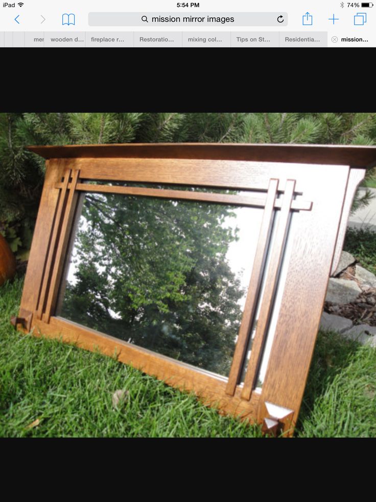 an old wooden mirror sitting on top of the grass in front of some rocks and trees