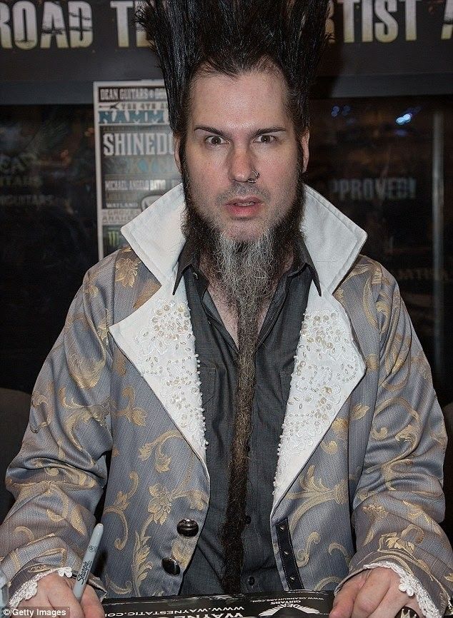 a man with black hair and beard sitting at a table in front of a sign