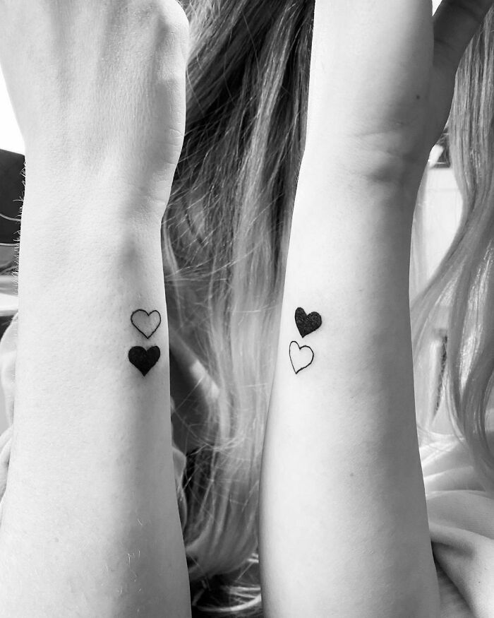 two women with matching tattoos on their arms and wrist, both have hearts tattooed on them