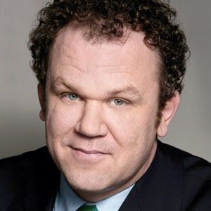 a man in a suit and tie with curly hair smiling at the camera while wearing a blue shirt and green tie