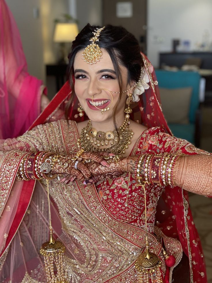 a woman in a red and gold bridal outfit is holding her hands out to the side