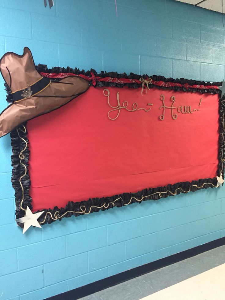 a red sign hanging from the side of a blue wall in a school hallway with a cowboy hat on it