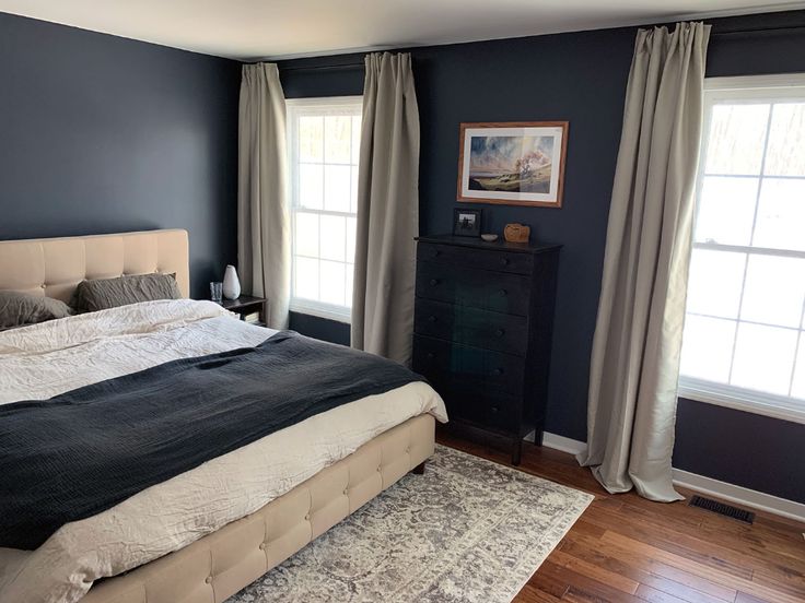 a large bed in a bedroom next to two windows with curtains on both sides and a rug on the floor