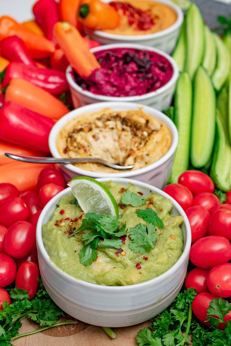 several bowls filled with guacamole, tomatoes, cucumbers and other vegetables