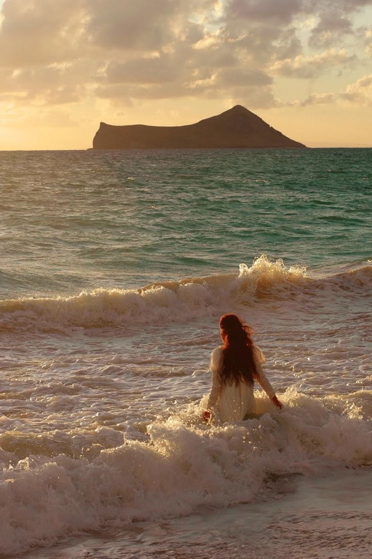 a woman sitting in the surf at sunset