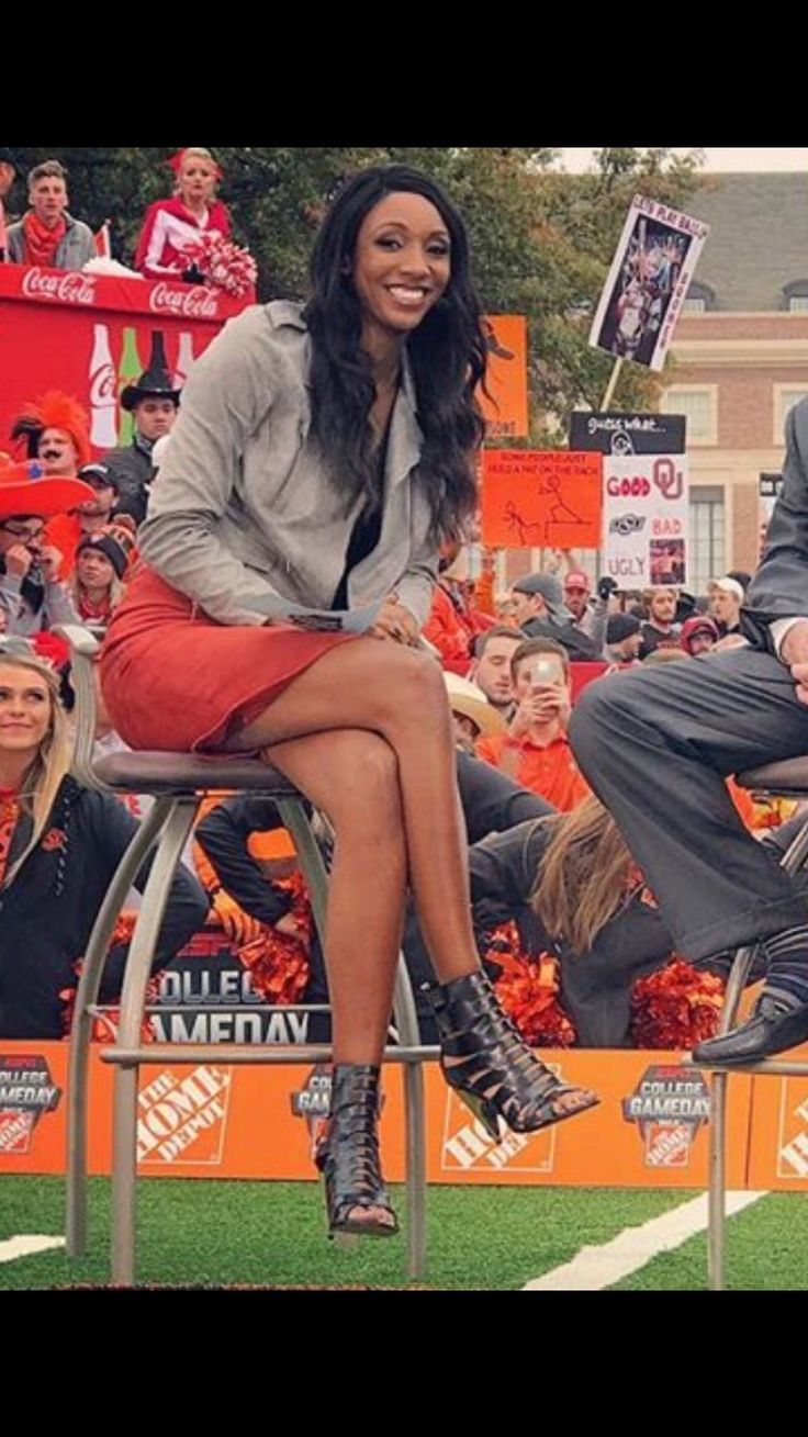 a man and woman sitting on chairs in front of an orange background at a football game