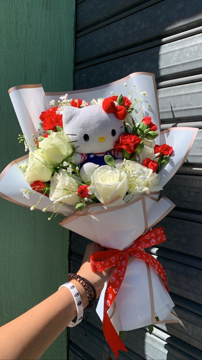 a hello kitty bouquet is being held by a woman's hand with red and white flowers