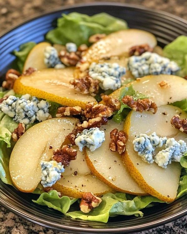 a salad with pears, blue cheese and walnuts in a bowl on a table