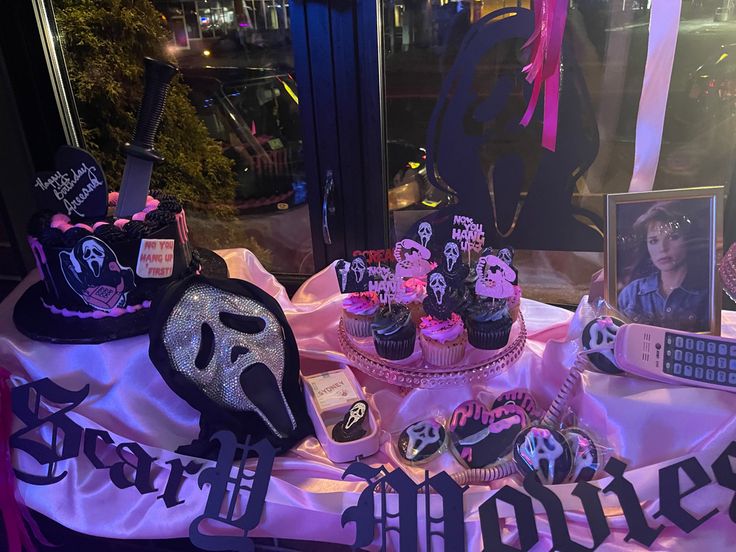 a table topped with cupcakes covered in black and pink frosting next to a window