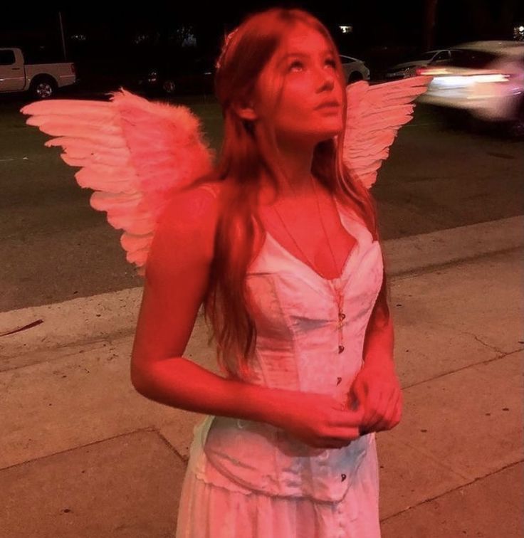 a woman in a white dress is standing on the sidewalk with an angel wings around her neck