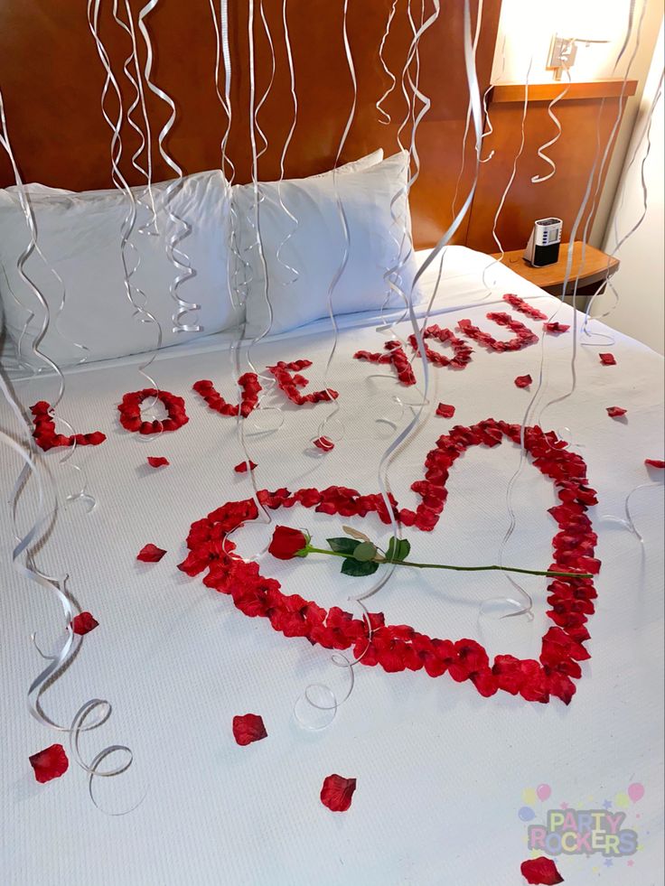 a bed with red rose petals and streamers in the shape of a love heart