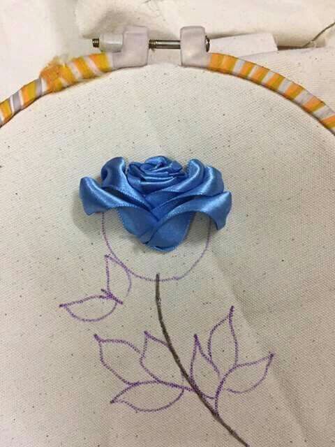 a close up of a blue rose on a white piece of cloth with stitching