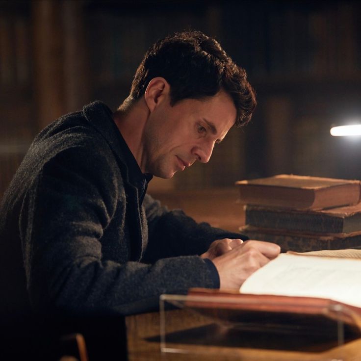 a man sitting at a desk writing on a piece of paper with a lamp in the background