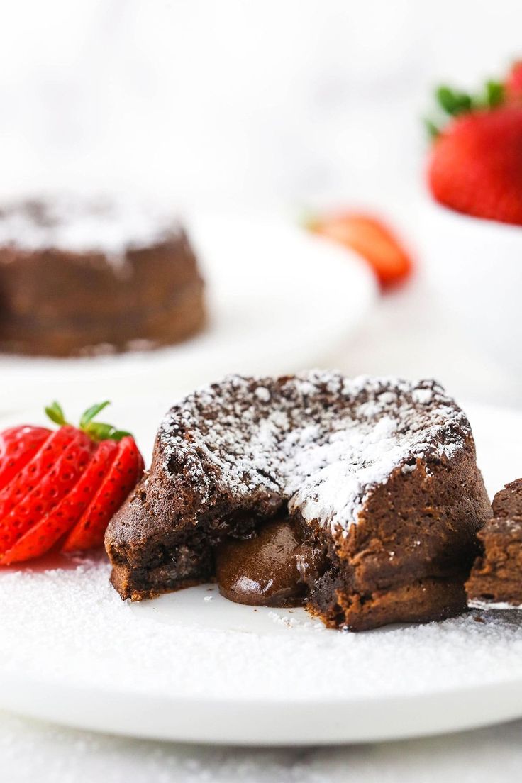 two pieces of chocolate cake on a white plate with strawberries and powdered sugar