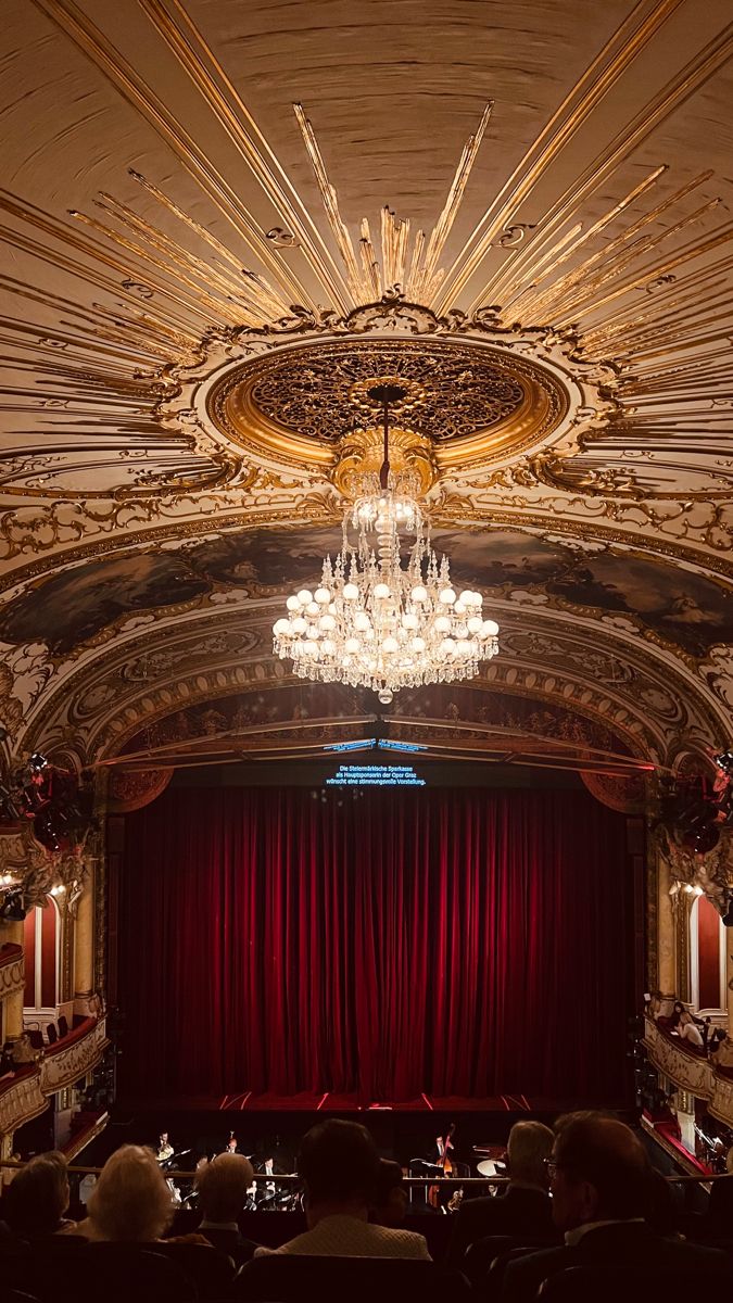 an ornately decorated auditorium with chandelier and red curtains