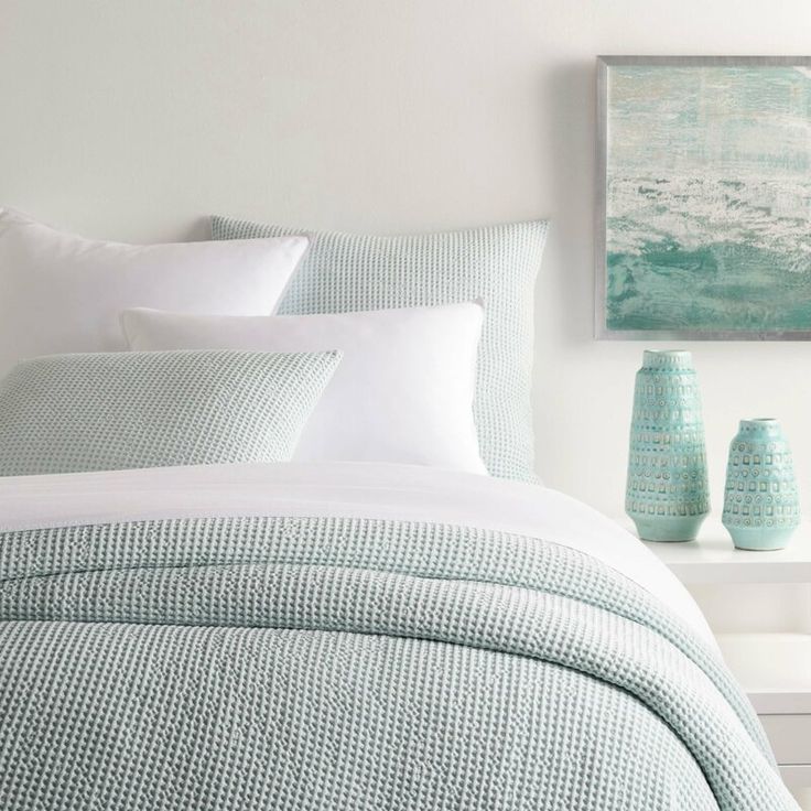 a bed with blue and white pillows in a bedroom next to a painting on the wall