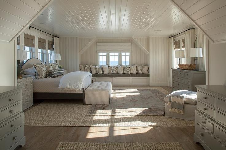 a large bedroom with white walls and wood flooring, along with two windows overlooking the ocean