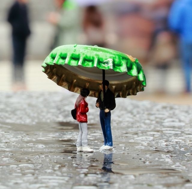 two miniature people under an umbrella on the ground