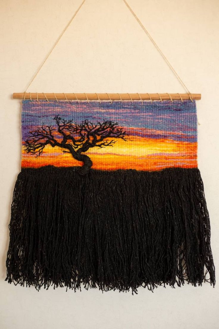 a tapestry hanging on a wall with a tree in the middle and an orange sunset behind it