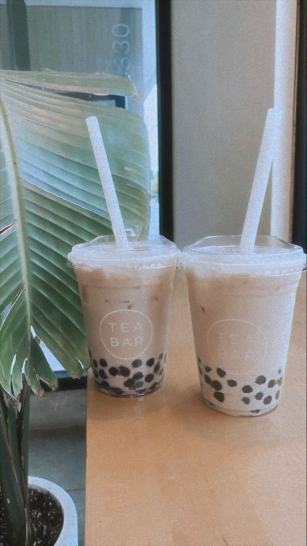 two cups with straws sitting on top of a table next to a potted plant