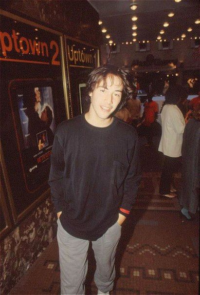 a young man standing in front of a movie poster at an indoor event with people walking around