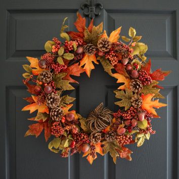 a wreath is hanging on the front door with autumn leaves and acorns around it