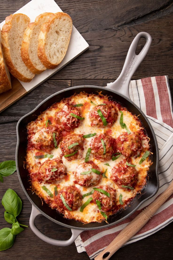 a skillet filled with meatballs and cheese on top of a table next to bread