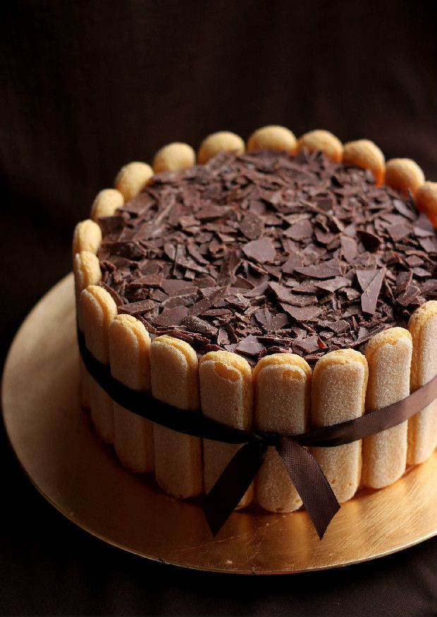 a chocolate cake on a plate with a brown ribbon around the edges and topped with chocolate shavings