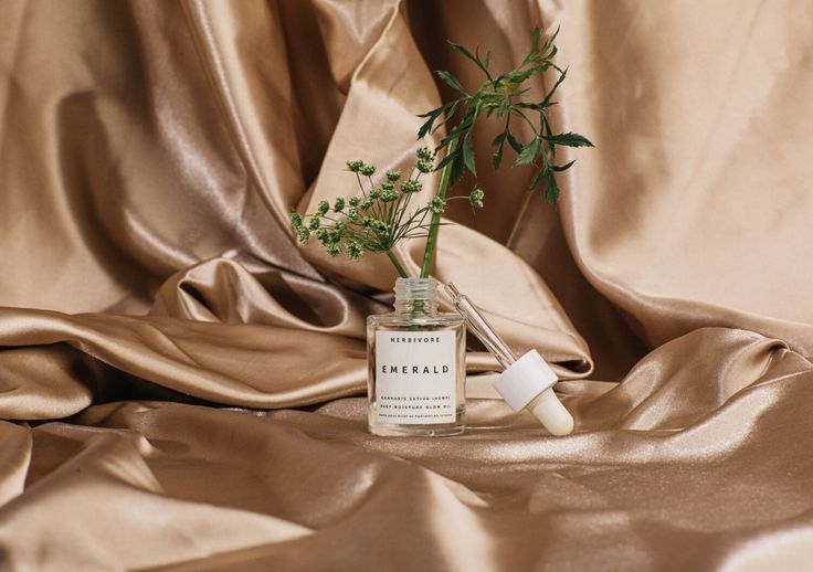 a bottle filled with green plants sitting on top of a satin covered table cloth next to a plant