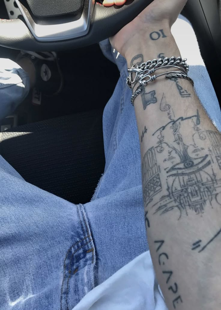 a person with tattoos on their arm holding a steering wheel and wearing a chain bracelet