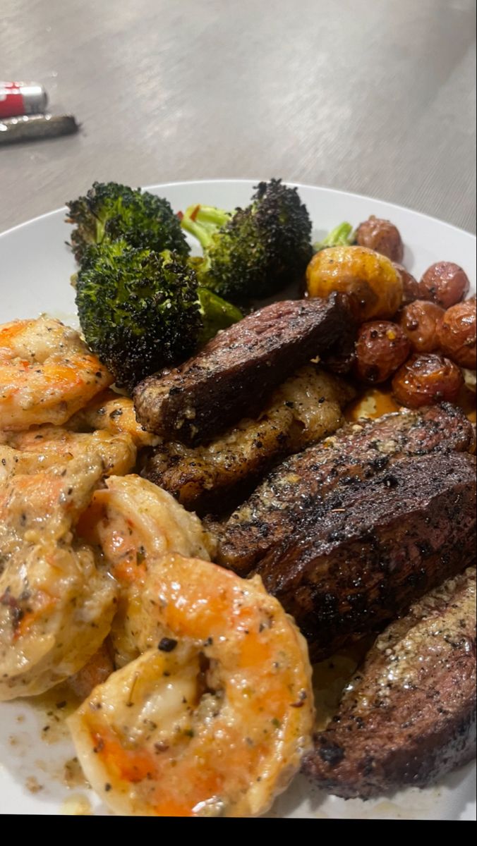 a white plate topped with meat, shrimp and broccoli next to a fork