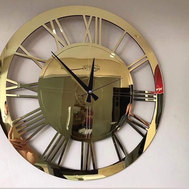 a gold clock with roman numerals on the face and mirror reflecting it's reflection