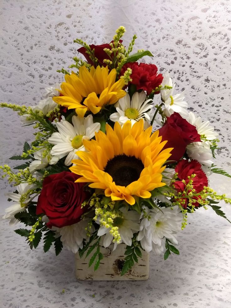 a bouquet of sunflowers, roses and other flowers in a vase on a table