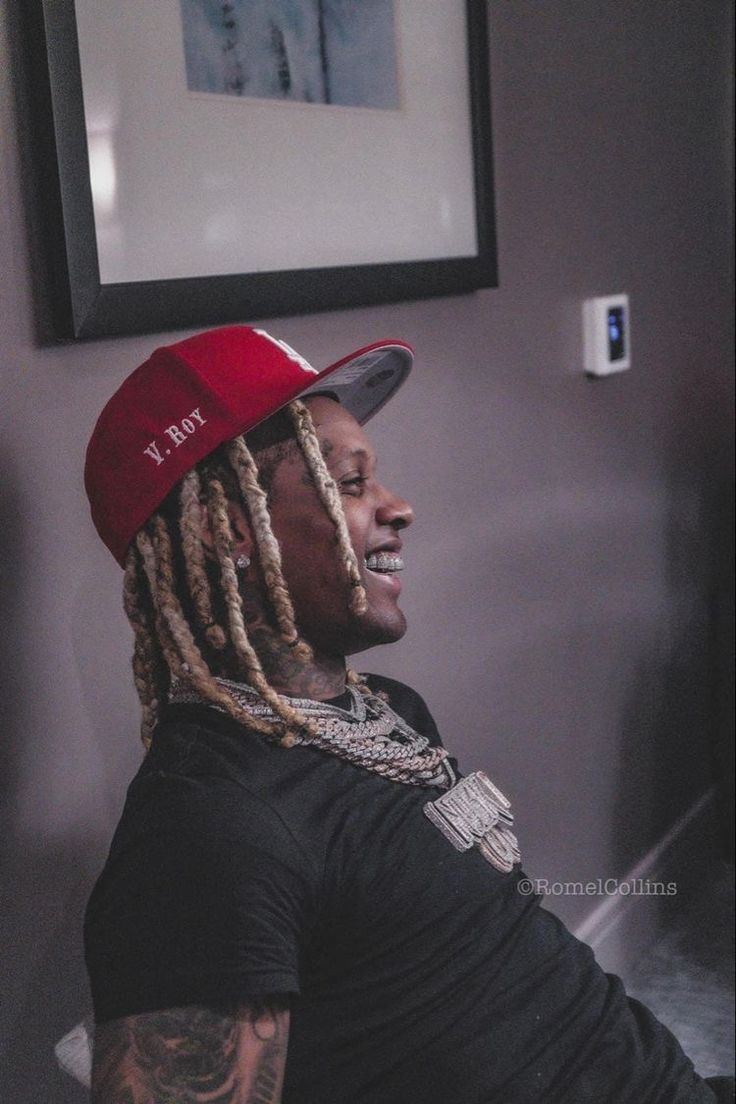 a man with dreadlocks and a red hat sitting in front of a wall