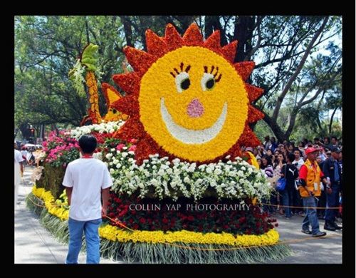 a man standing in front of a float with flowers on it's head and smiling face