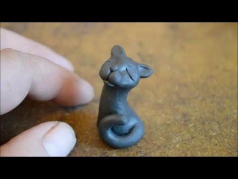 a tiny cat figurine sitting on top of a table next to a person's finger