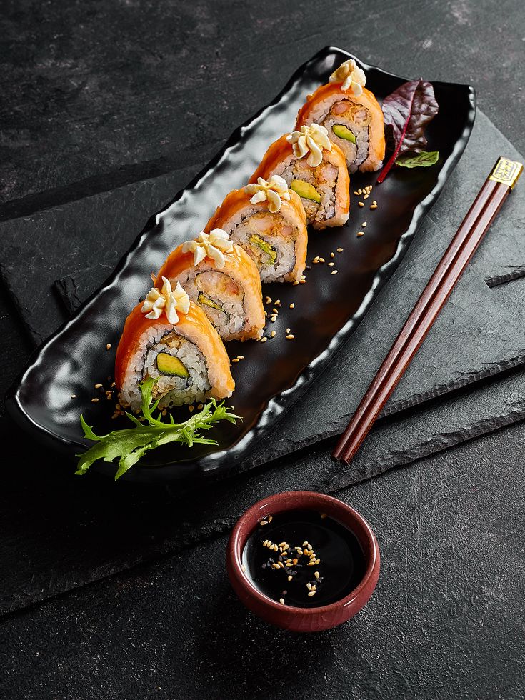 sushi rolls on a black plate with chopsticks next to it and dipping sauce