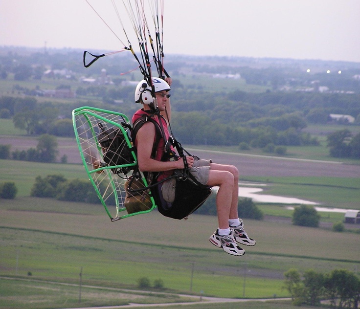 a man riding on top of a parachute over a lush green field