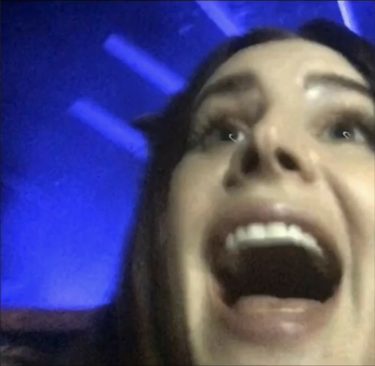 a woman with her mouth open in front of a blue background and lights on the ceiling