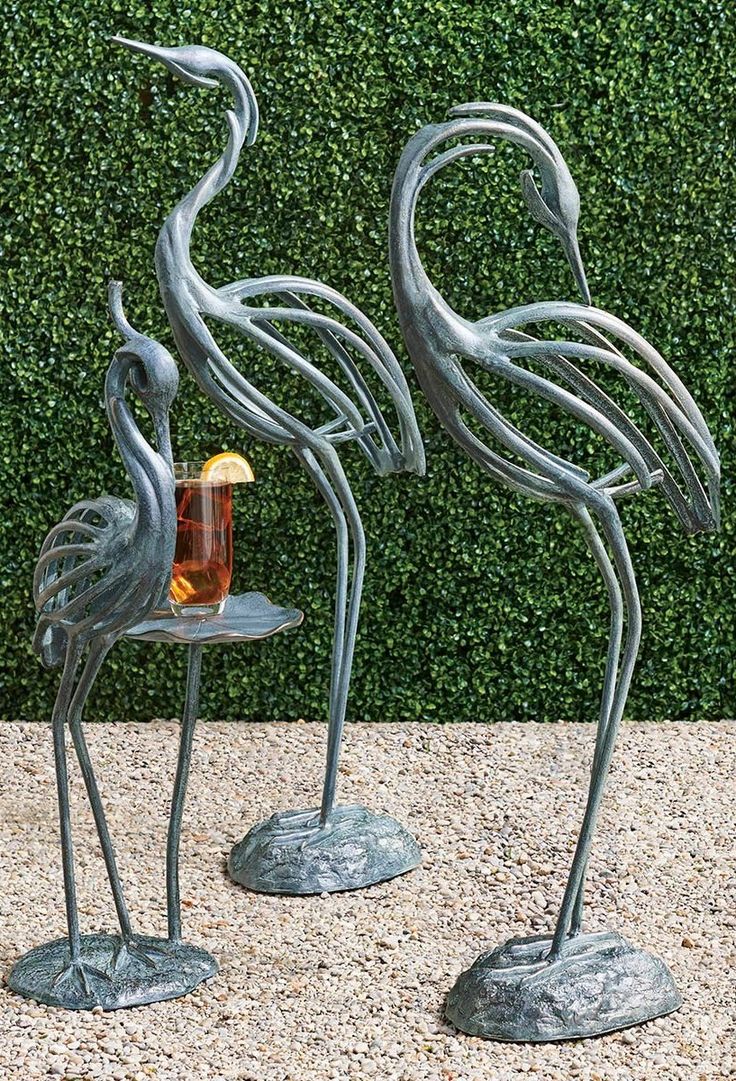 two metal flamingos standing next to each other with a drink in their beaks