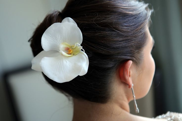 a close up of a woman with a flower in her hair, wearing earrings and a white dress