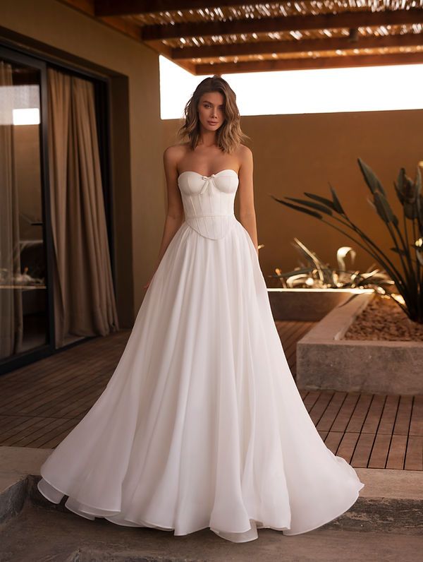 a woman in a white wedding dress standing on a patio with her hands behind her back