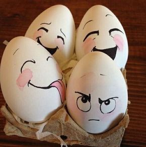 four eggs with faces drawn on them sitting in an egg carton